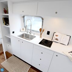 a kitchen with white cabinets and an open book on the counter top next to a sink