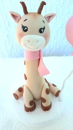 a giraffe figurine sitting on top of a white surface next to a pink balloon