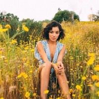 a woman sitting in the middle of a field with yellow flowers on it's side