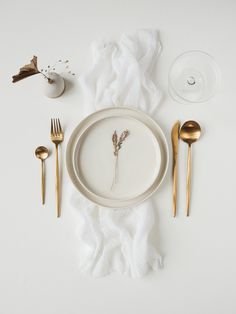 a white plate topped with a dried flower next to gold utensils and napkins