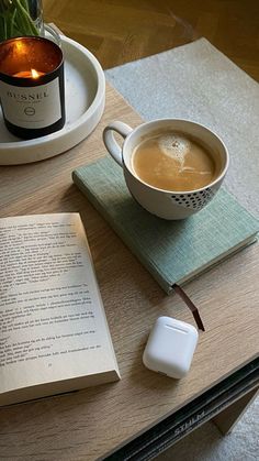 an open book sitting on top of a wooden table next to a cup of coffee