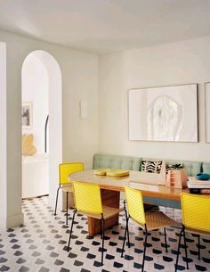 a dining room table with yellow chairs and artwork on the wall