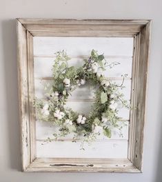 an old frame with a wreath hanging on the wall next to a white painted wall