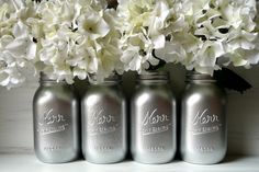 three silver mason jars with white flowers in them