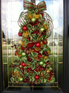 a christmas tree made out of green and red ornaments in front of a glass door