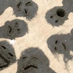 several people are standing in the sand with their faces drawn on them and there is a person's shadow