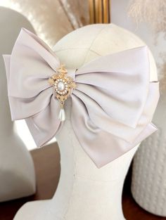 A beautiful champagne hair bow barrette with a gold Victorian style brooch and faux pearls.  *DETAILS*  * The bow is attached to a silver french Barrett hair clip * measurements - 21cm across 14cm down.  * your bow will arrive in a gift box with luxury ribbon.  *DELIVERY DEATAILS* All UK orders are sent via the Royal Mail 1st Class Signed for service. All international orders are sent via a Tracked and Signed service where possible. SHOP MORE STYLES: Honeyandember.etsy.com/ FIND ME ON: www.insta Elegant Pre-tied Satin Bow, Elegant Satin Ribbon Bow, Cottagecore Hair, Elegant Cream Satin Bow, Elegant Adjustable Bow Hair Accessories, Champagne Hair, Adjustable Red Satin Bow, Princess And The Pauper, Princess Inspired