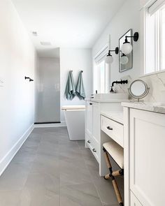 a long bathroom with white cabinets and gray tile flooring, along with two mirrors on the wall