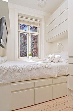 a bedroom with white furniture and a flat screen tv mounted to the side of the bed