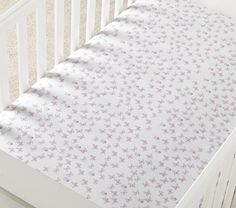 a white crib bed with purple flowers on the sheets and bottom sheet that is folded down