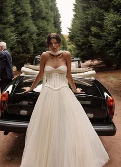 a woman in a wedding dress standing next to a car