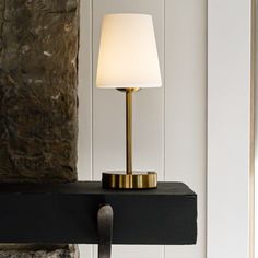 a lamp on a black shelf next to a stone wall and window sill in a living room