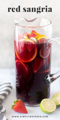 a pitcher filled with red sangria sitting next to sliced lemons and strawberries