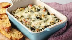 a casserole dish with cheese and spinach in it next to slices of bread