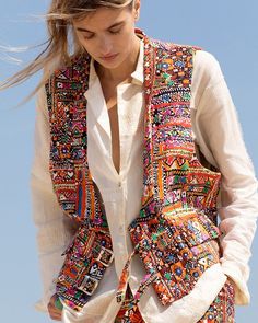 A person wearing a white dress and the Lucien Banjara Vest, which features a vibrant, intricately patterned design, stands against a clear blue sky. Their hair gently blows in the wind as they look downwards, showcasing the relaxed fit and hand-printed cotton details of their scoop neck ensemble. Purple Lace Midi Dress, Resort 23, Alix Of Bohemia, Hand Printing, Latest Bridal Dresses, Elegant Outfit Classy, Fashion Line, Lace Midi Dress, A Style