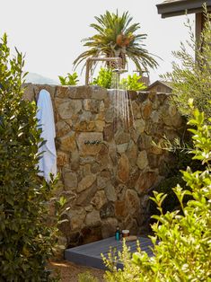 a stone wall with a shower head in the middle and some plants around it on either side