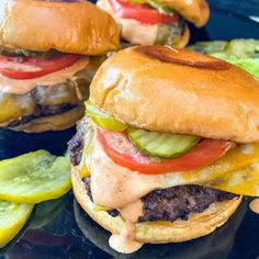 three hamburgers with cheese, tomatoes and pickles on them