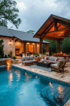 an outdoor living area next to a swimming pool with lounge chairs and lights on the patio