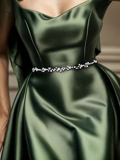 a woman in a green dress with a crystal belt on her waist and hand behind her back