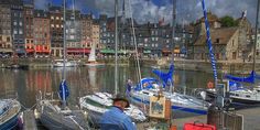 a man sitting on a chair in front of boats docked at a harbor with buildings in the background