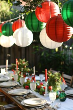 an outdoor table set for christmas dinner with paper lanterns hanging from the ceiling and place settings