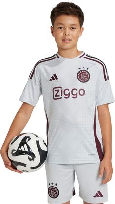 a young boy holding a soccer ball and wearing a white shirt with maroon trims