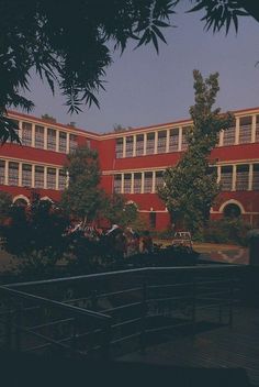 the building is red and white with many windows on each side, along with several trees in front of it