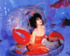 a woman is sitting in the water surrounded by fish and corals, with her hair blowing back