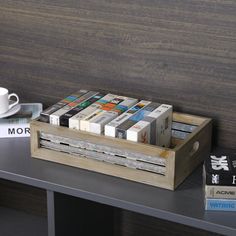 a wooden box filled with lots of books next to a coffee cup and book on a table