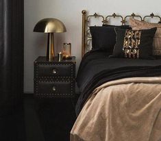 a bed with black and gold pillows on it next to a night stand in a bedroom