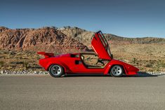 a red sports car with its doors open on the road in front of some mountains