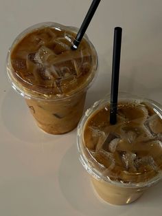 two plastic cups filled with ice cream and brown liquid sitting next to each other on a white surface