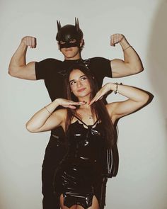 a man standing next to a woman wearing a cat mask and latex outfit with her hands behind her head