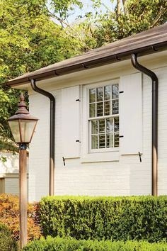 a white house with a lamp post in front of it and shrubbery around the corner