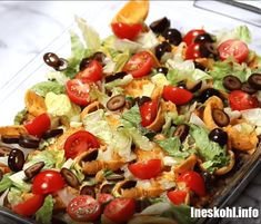 a salad with tomatoes, olives and lettuce in a glass dish on a marble countertop