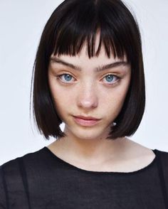 a close up of a person with a short haircut and blue eyes wearing a black shirt