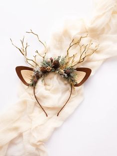 a cat headband with branches and pine cones is on top of a white cloth