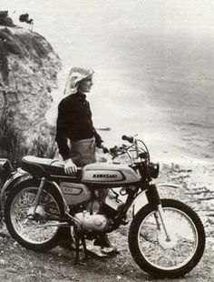 a woman standing next to a motorcycle on top of a rocky hill near the ocean