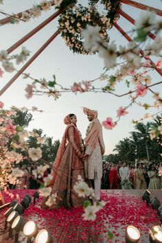 two people standing next to each other under a canopy with flowers on the ground and candles in front of them