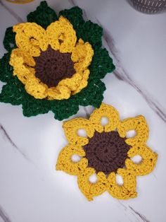 two crocheted flowers sitting on top of a white table next to each other