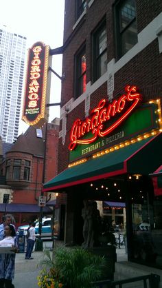 people are walking on the sidewalk in front of a building with neon signs and lights