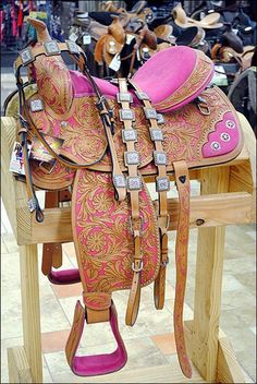 a pink and gold saddle sits on a wooden stand