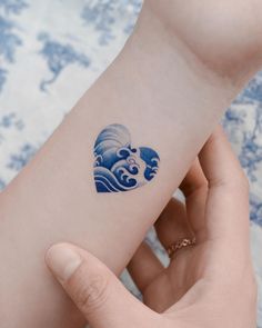 a small blue wave tattoo on the left inner arm and wrist, with an ocean wave coming out of it