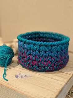 a crocheted basket sitting on top of a wooden table next to a ball of yarn