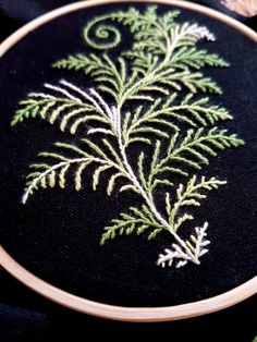 a close up of a embroidery on a black cloth with green and white leaves in it