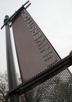 a large metal sign on top of a pole near a street light and some trees