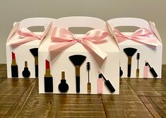 three white boxes with pink bows and various makeup items in them on a wooden floor