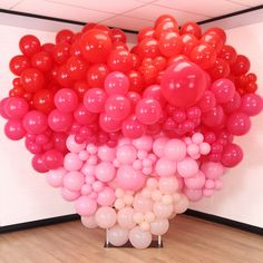 a bunch of red and pink balloons in the shape of a tree on a wooden floor