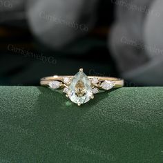 an engagement ring with two pear shaped diamonds on the front and side, sitting on a green surface