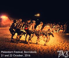 a group of people are running around in the sand at night with fireworks behind them